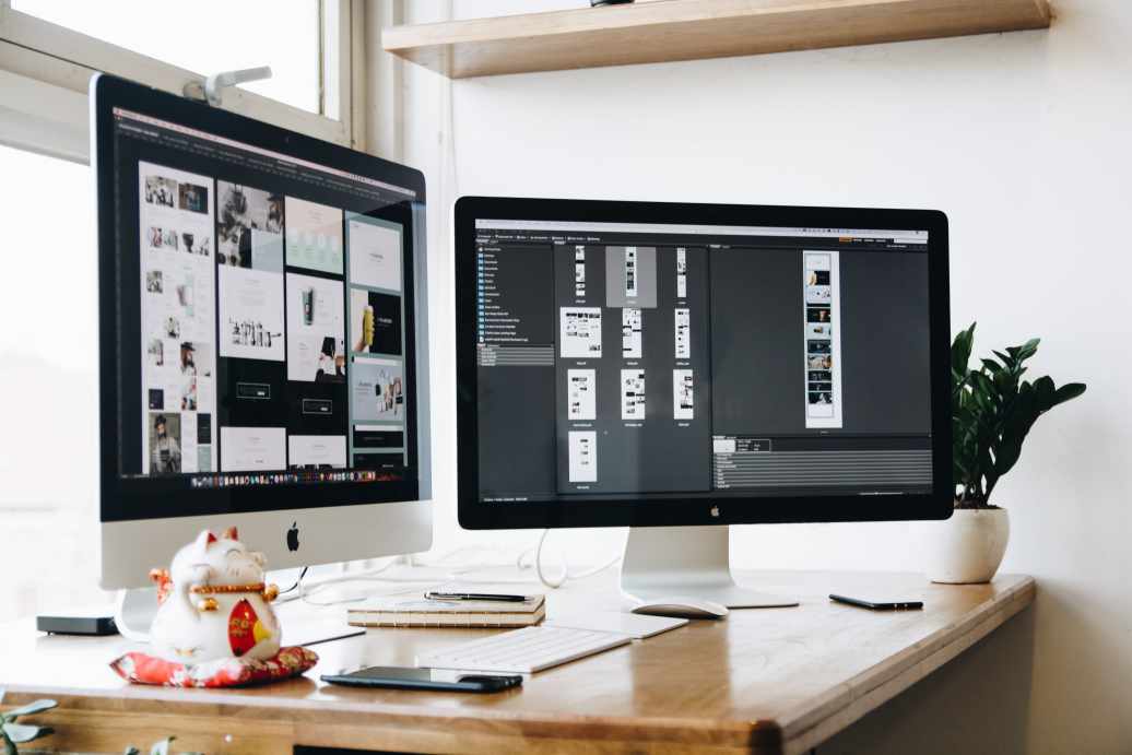 Outsourcing Graphic Design: Your Massive Guide this 2021 10 Two iMacs on a table working layouting of a print design for graphic design outsourcing.
