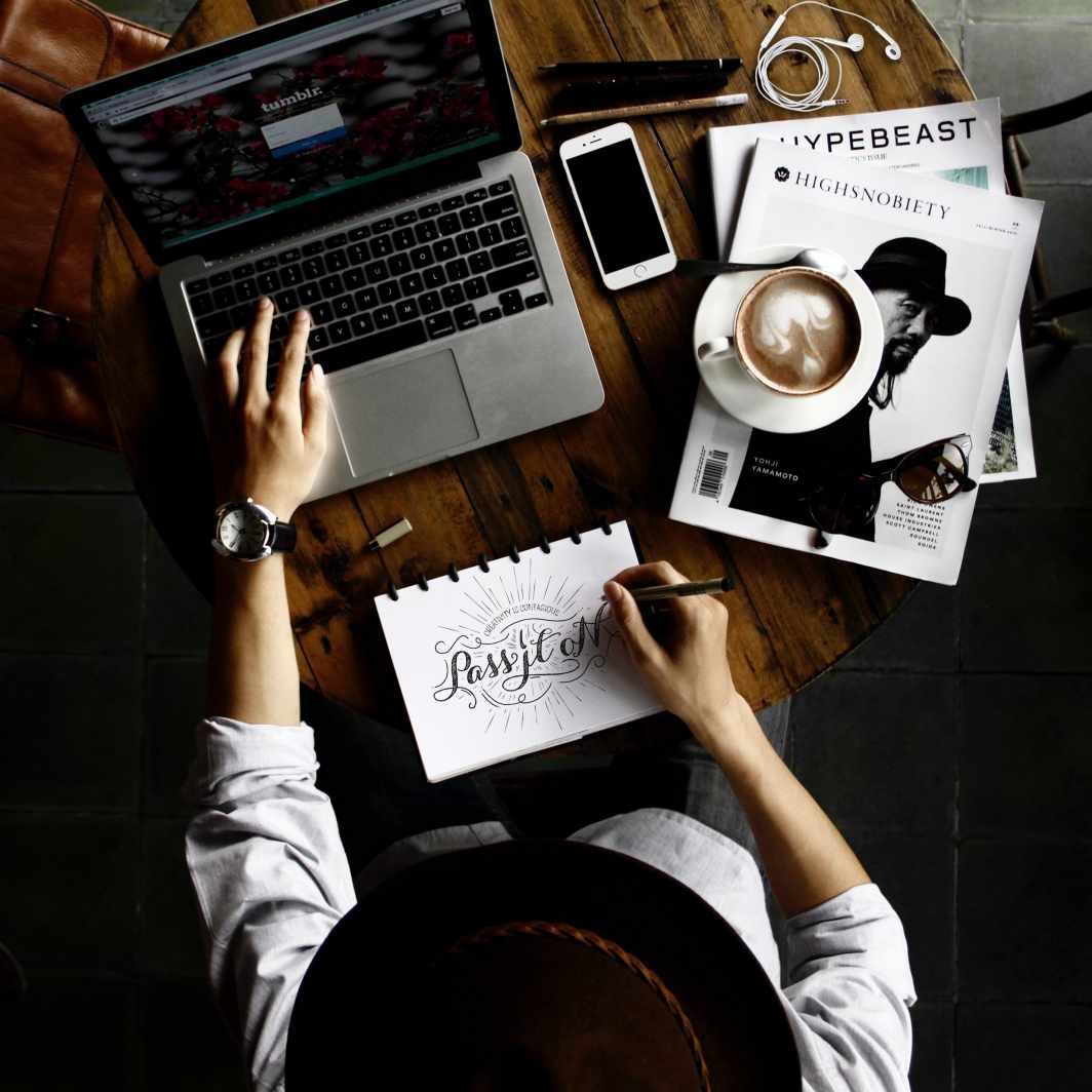 Outsourcing Graphic Design: Your Massive Guide this 2021 8 Top view of a person outsourcing graphic design in a laptop, notebook, magazine, and coffee. -