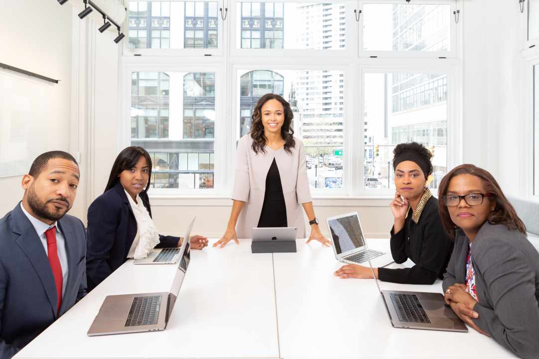 Outsourcing Graphic Design: Your Massive Guide this 2021 7 Five people, four sitting and one standing, asking who should outsource graphic design services.